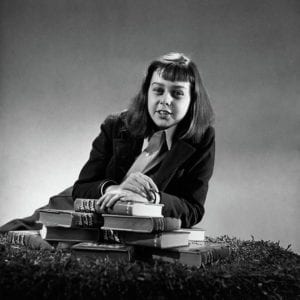 em preto e branco, autora bem jovem debruçada sobre pilha de livros