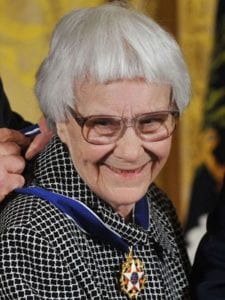 autor abem idosa de cabelos curos e brancos com casaco xadrez preto e branco, recebendo uma medalha