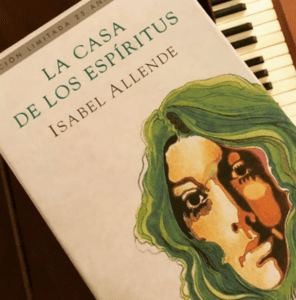 capa branca com desenho aquarelado de um rosto feminino de cabelos verdes. o livro repousa sobre um piano e as teclas se veem ao fundo