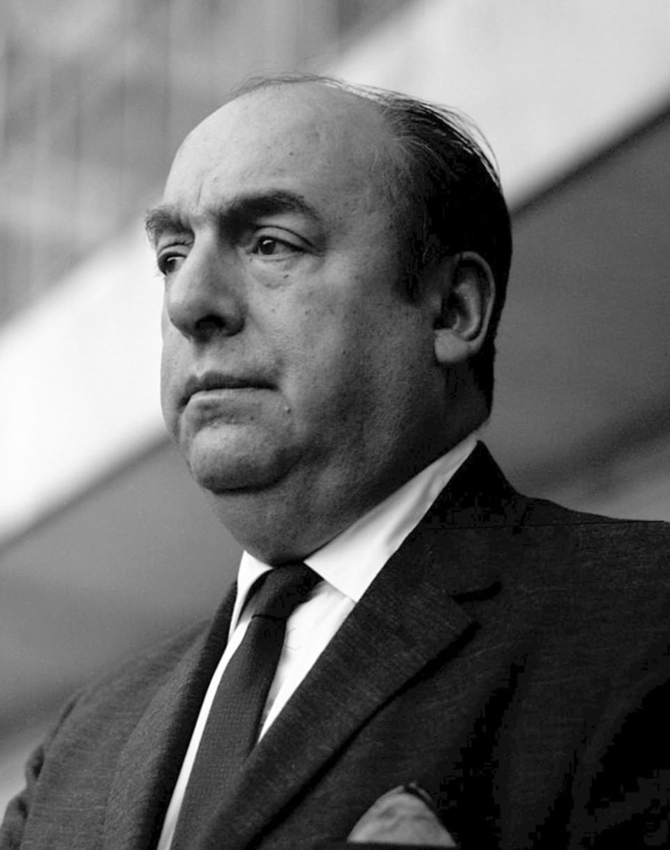 Foto em preto e branco. Pablo Neruda, na meia idade, de terno e gravata escuros e camisa clara, de perfil 3/4